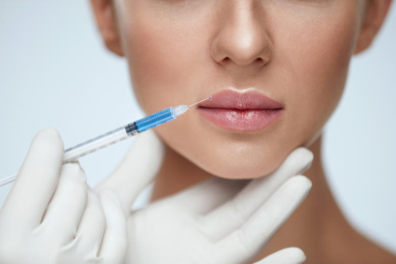 Lippen einer schönen Frau werden mit einer Hyaluronsäurespritze behandelt.